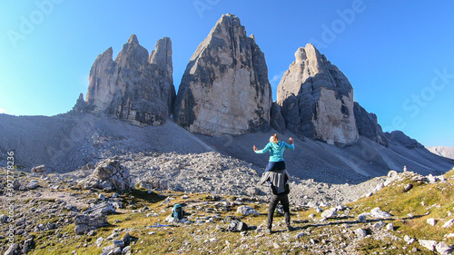 Man carrying woman piggyback with the close up view on the Tre Cime di Lavaredo (Drei Zinnen) in Italian Dolomites. Sharp and high mountain wall. Desolated and raw landscape. Fun and careless moments