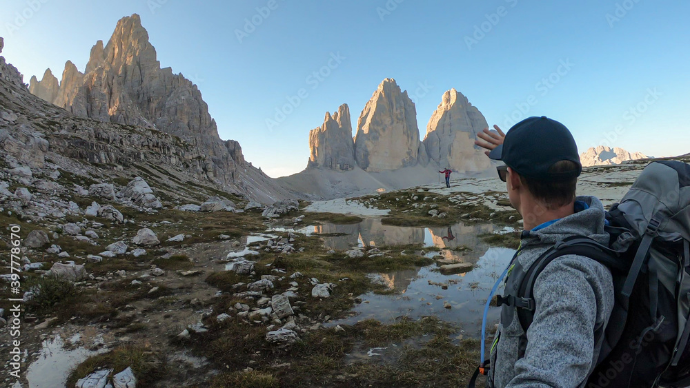 A couple taking a selfie with the Tre Cime di Lavaredo (Drei Zinnen), mountains in Italian Dolomites. The mountains are reflecting in small paddle. Desolated and raw landscape. Early morning. Daybreak