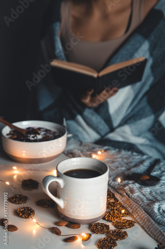 The woman is wrapped in a blanket and holds a book in her hands. cup of coffee . 