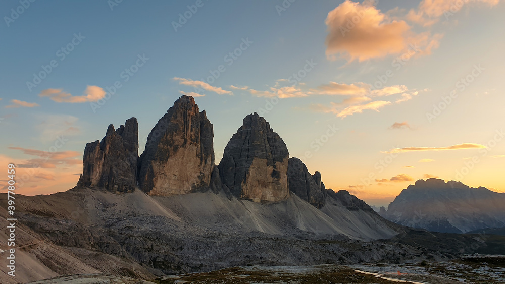Golden hour over famous Tre Cime di Lavaredo (Drei Zinnen), mountains in Italian Dolomites. The mountains are surrounded with orange and pink clouds. Desolated and raw landscape. Sunset time. Serenity