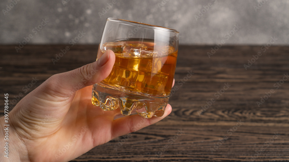 Hand holding glass of brown rum with ice cubes on rustic wooden table with copy-space Hand holding glass of brown rum with ice cubes on rustic wooden table with copy-space