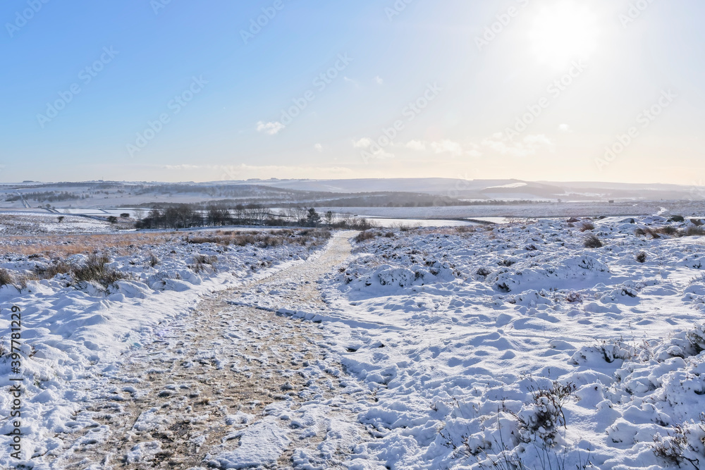 A frozen footpath over a snow covered Derbyshire landscape lit by a low winter sun