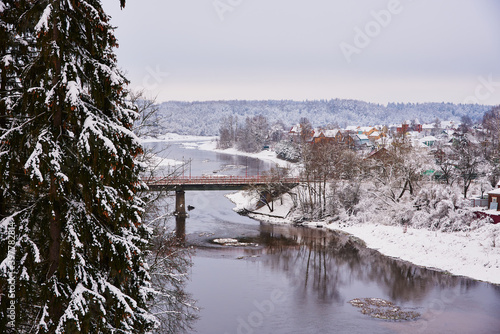  A snow-covered village on the Bank of a river that is crossed by a road bridge.