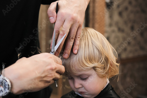 A little boy is trimmed in the barbershop. Bright emotions on the face, facial expression, the process of cutting hair.