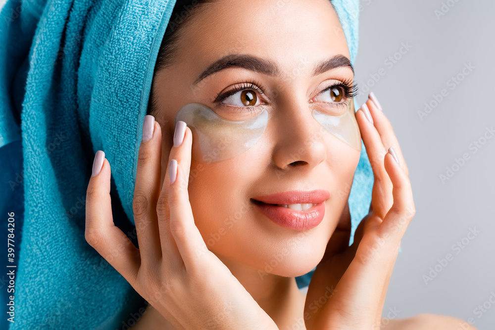 smiling beautiful woman with blue towel on hair and hydrogel eye patches on face isolated on grey smiling beautiful woman with blue towel on hair and hydrogel eye patches on face isolated on grey
