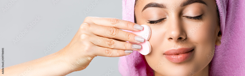 beautiful woman cleaning face with heart shaped sponge isolated on grey, banner