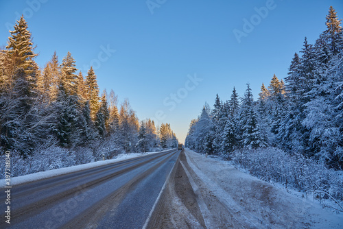 Car paved road in the middle of a snow-covered forest under a bright blue sky.