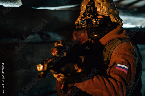 Russian spetsnaz soldier with Kalashnikov tactical assault rifle with night-vision device in dark room. Text on sleeve translation: Russia.
