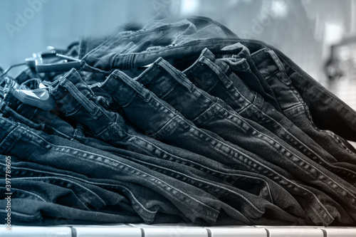 Piles of jeans on a shelf in a store, close-up, selective focus, front view, tinted blue. Shopping clothes concept