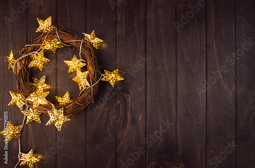 Fashion glittering festive decoration -  wreath with golden glowing stars on dark brown wood board  border  top view.