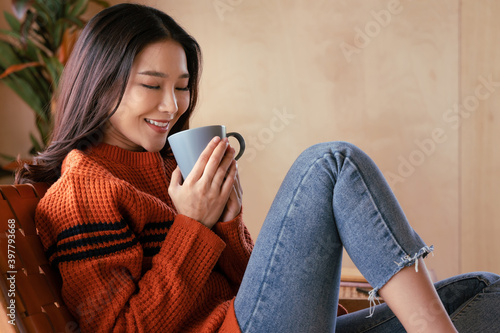 Portrait of a young Asian woman wearing a sweater. She inhaled the scent and drank the winter morning coffee. She smiles and enjoys being relaxed at home.