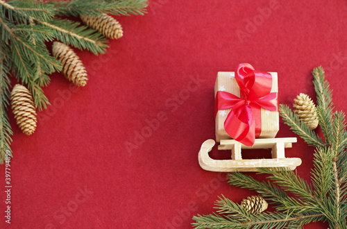 Christmas greeting background with a gift box tied with a ribbon, on a small toy sled, surrounded by fir branches. Red felt background.Place for text.