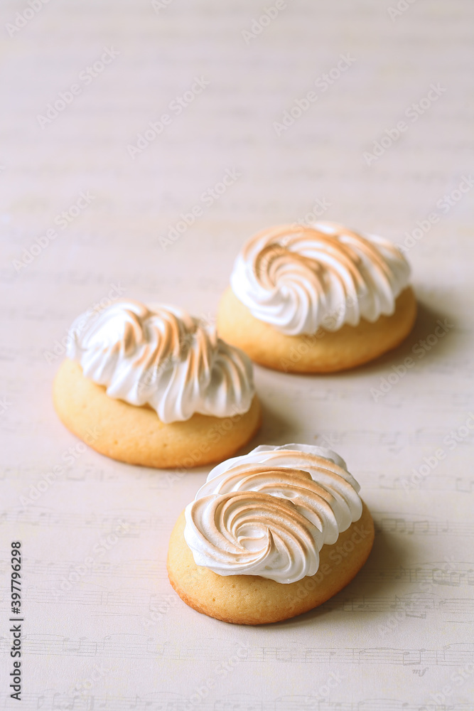 Butter Cookies with Lemon Curd and topped with Burnt Italian Meringue, on a light beige background.