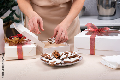 Female hands are wrapping gingerbread cookies in gift box. Christmas box. Close up.