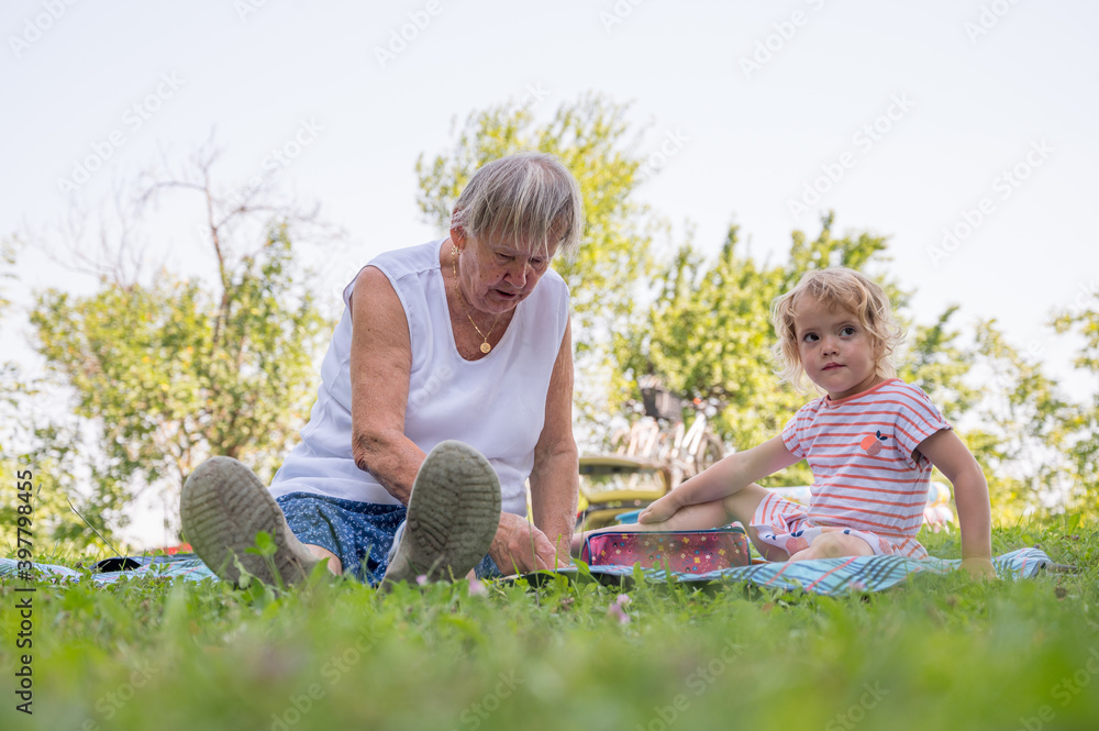 Grandmother with her grandaughter casually sitting on a blanket reading and talking in a park. Grandmother with her grandaughter casually sitting on a blanket reading and talking in a park.