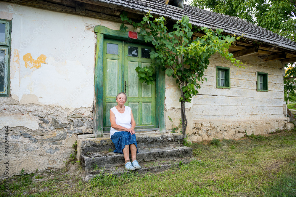 Elder woman sitting at the steps of old house and remembering.