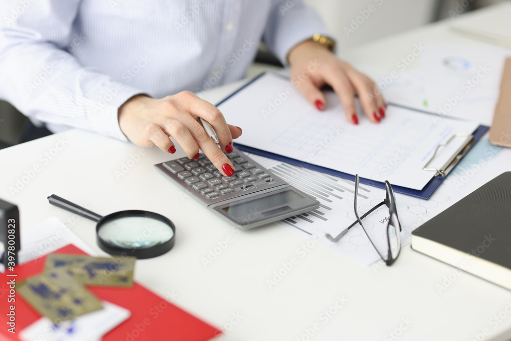 Fototapeta premium Business woman with red manicure counting on calculator in office closeup