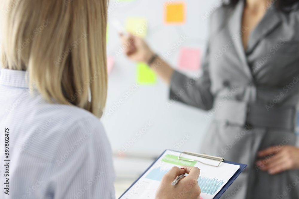 Woman looking at graph on clipboard. Director pointing with pen to board Woman looking at graph on clipboard. Director pointing with pen to board