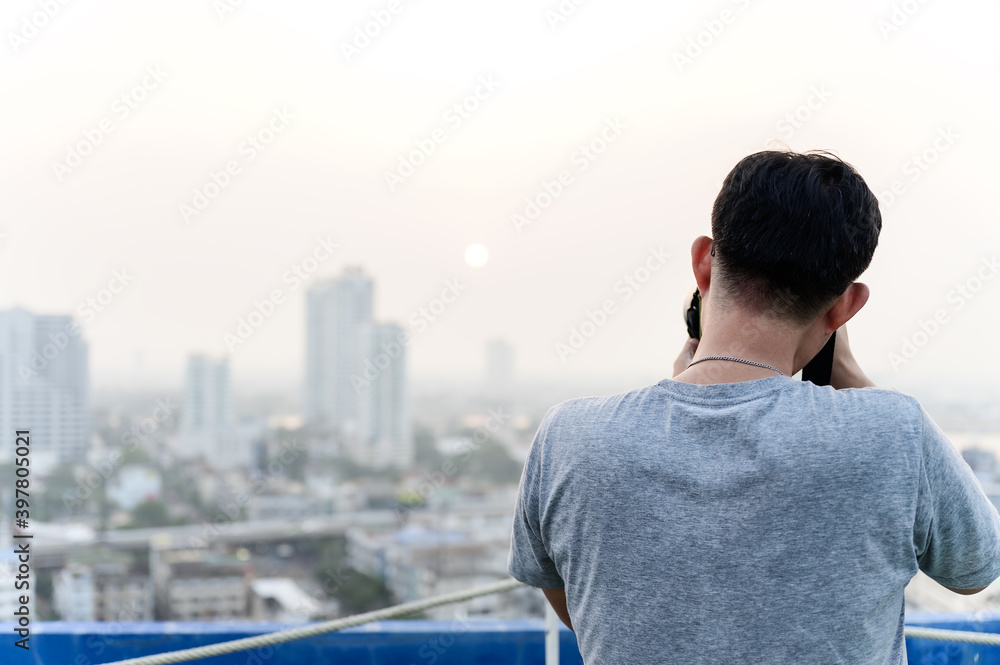 Fototapeta premium Asian photographer man is using his Dslr or mirrorless camera to take pictures of cityscape with the Sunrise or sunset