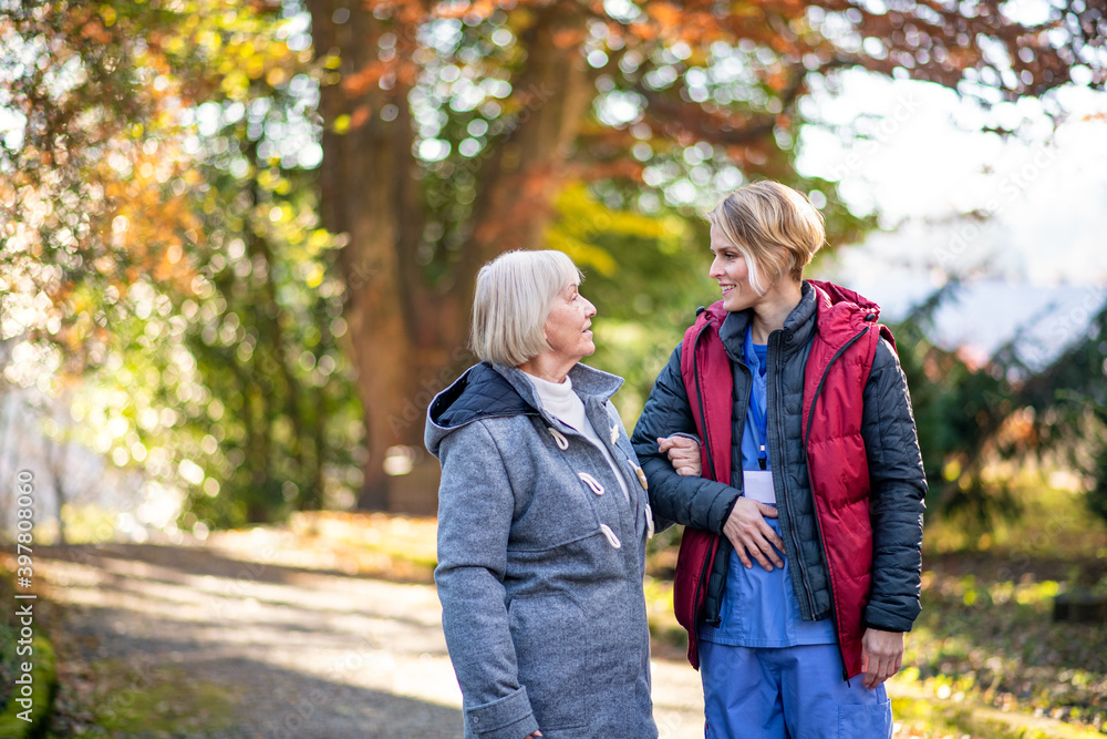 Senior woman with caregiver outdoors on a walk in park, coronavirus concept. Senior woman with caregiver outdoors on a walk in park, coronavirus concept.