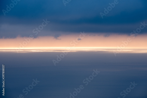 surface de mer bleu gris avec une ligne horizontale de lumière à l'horizon sous des nuages gris bleus © Christophe