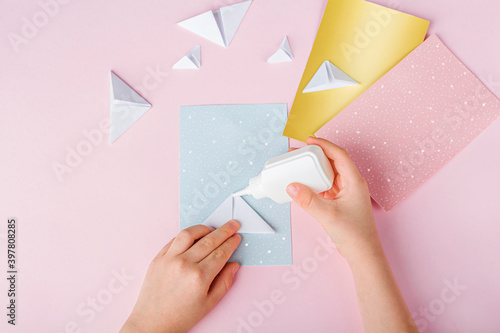 Concept of DIY and kid's creativity, origami. Step by step instruction: how to make greeting cards with christmas trees origami. Step5 Glue the triangles to postcard. New year craft photo