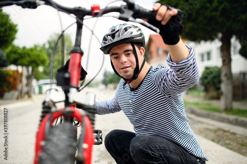 Portrait of down syndrome adult man with bicycle standing outdoors on street.