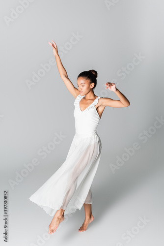 barefoot graceful african american ballerina in dress dancing on white background