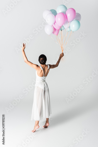 barefoot graceful african american ballerina in dress dancing with balloons on white background
