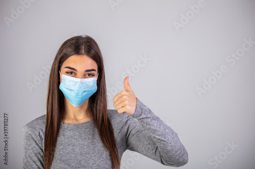 Beautiful caucasian young woman with disposable face mask. Protection versus viruses and infection. Studio portrait, concept with white background. Woman showing thumb up.