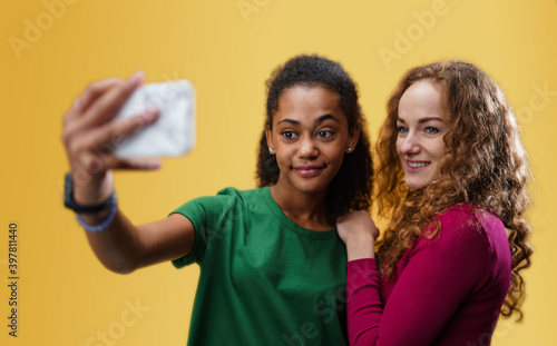 Young woman with teenager girl in a studio on yellow background  taking selfie.