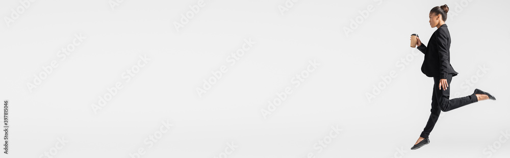 side view of african american businesswoman performing ballet with paper cup isolated on grey, banner side view of african american businesswoman performing ballet with paper cup isolated on grey, banner