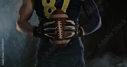 American football sportsman player holding a ball on black background close up