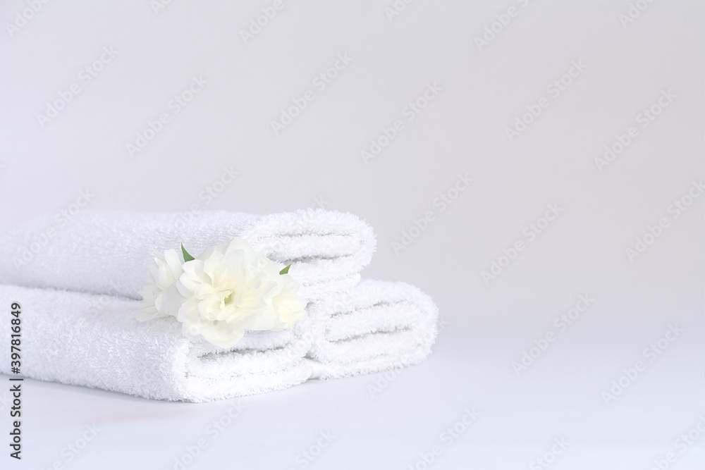 Three white neatly folded terry towels with a jasmine flower on a light background. Three white neatly folded terry towels with a jasmine flower on a light background.