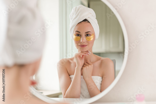 Young beautiful woman with silicone gold eye patches. Facial care at home. Girl with clean skin. Young beautiful girl cares for the skin using patches under the eyes at home.