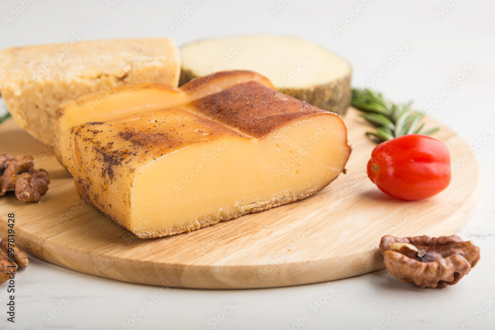 Smoked cheese and various types of cheese with rosemary and tomatoes on wooden board on a white background . Side view, selective focus.