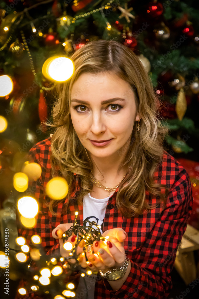 Girl with lights sitting on the background of Christmas tree at home, Happy New Year 2021 Girl with lights sitting on the background of Christmas tree at home, Happy New Year 2021