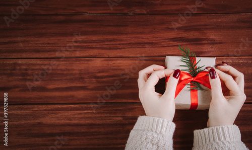 Christmas gift wrapping process. Woman decorates box with red ribbon.