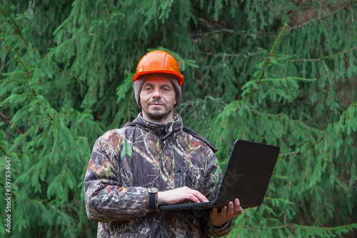 Forest engineer working in the forest with a computer. 40 years old man looking at the camera. Forestry and forest inventory. Real people work.