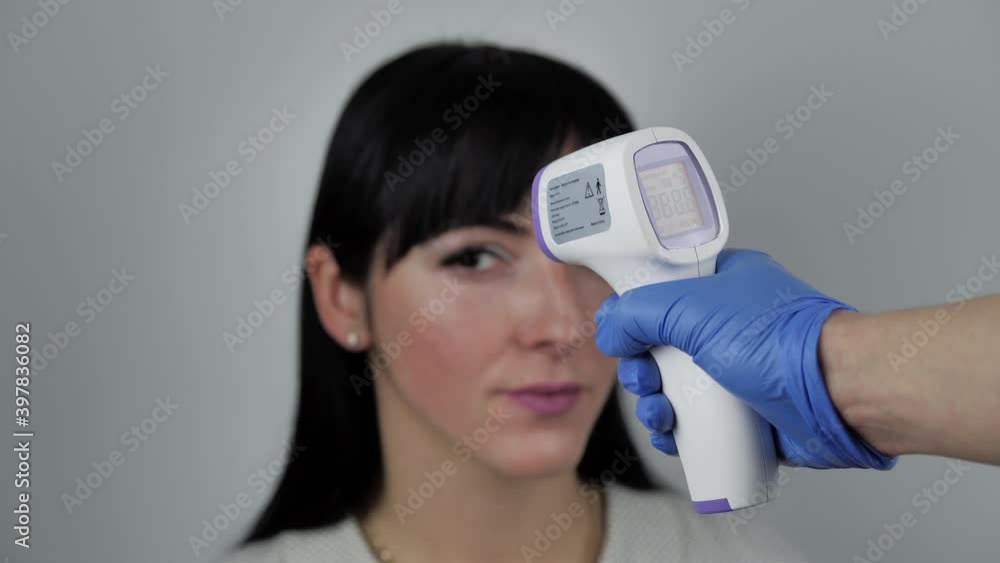 Close up video of contactless thermometer used to check temperature brunette young female. Focus on pistol silhouette blurred female in the background Close up video of contactless thermometer used to check temperature brunette young female. Focus on pistol silhouette blurred female in the background