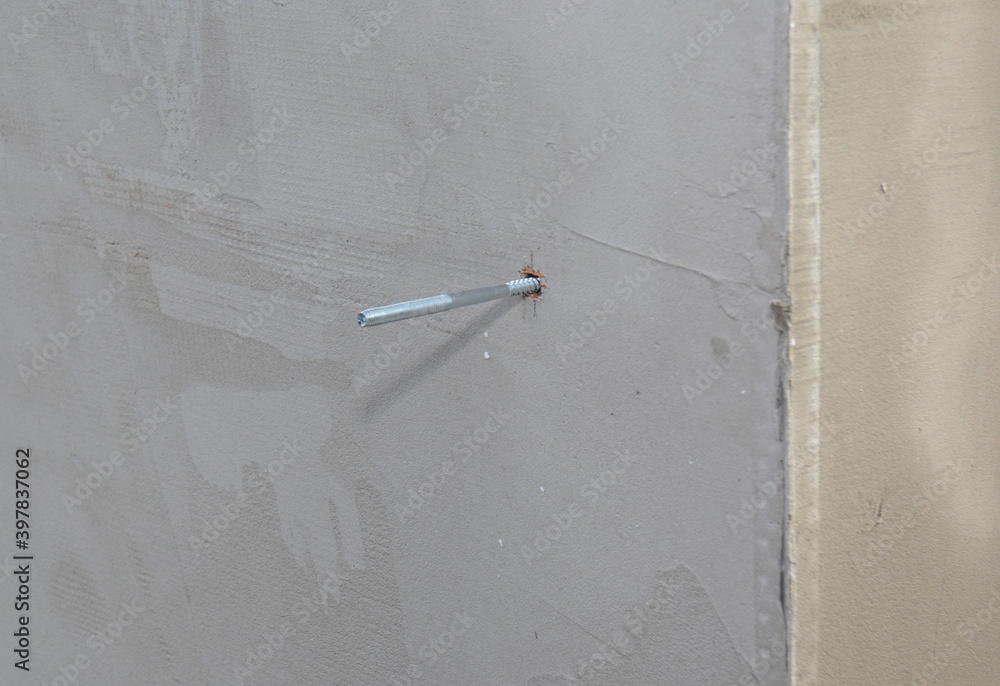 A closeup on a metal screw anchor, bolt anchor, metal fastener, screwed in a concrete wall with