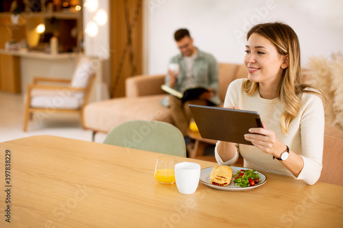 Young woman using digital tablet and having breakfast in the kitchen