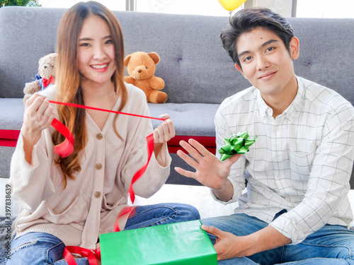 Asian young woman and man lover decorating Christmas tree and gift boxes spending happy time during traditional Christmas holiday festival. 