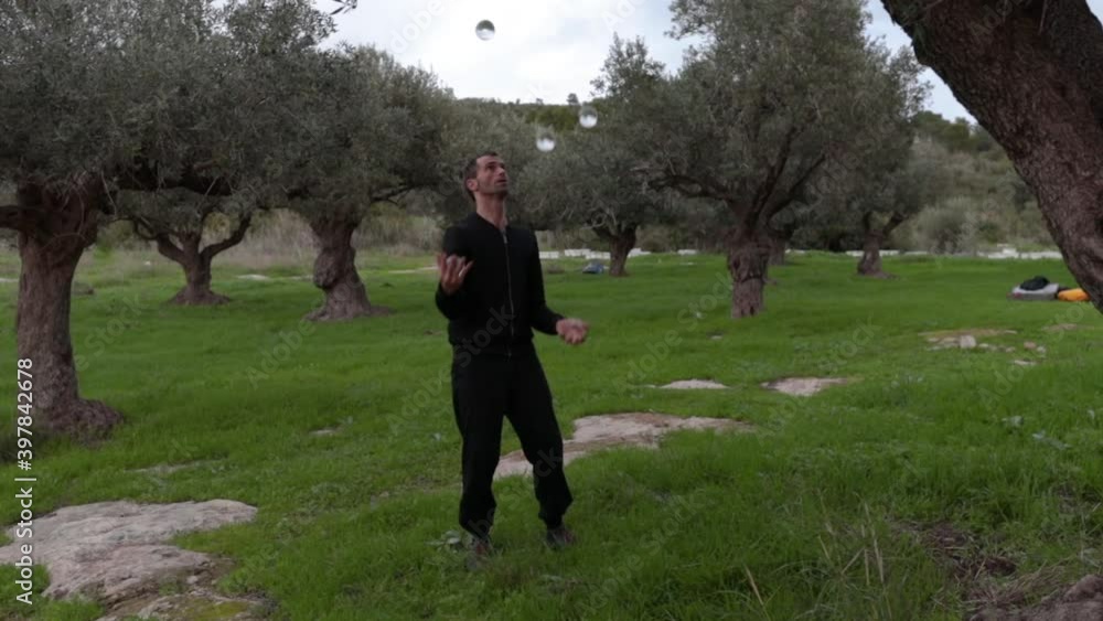 Circus artist juggling 4 transparent balls. Slow motion wide shot with olive trees in the background. Circus artist juggling 4 transparent balls. Slow motion wide shot with olive trees in the background.
