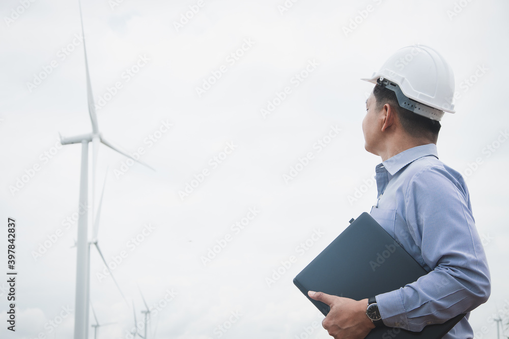 Engineers windmills are working on laptop with the wind turbine in background Engineers windmills are working on laptop with the wind turbine in background