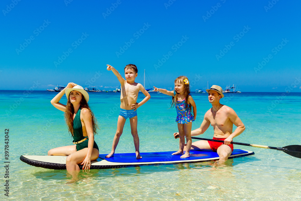 Happy family-mom, dad, little girl and boy have fun on a paddleboard in the tropical sea. The concept of travel and family holidays. Happy family-mom, dad, little girl and boy have fun on a paddleboard in the tropical sea. The concept of travel and family holidays.