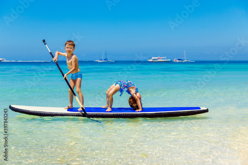 Smiling little girl and boy having fun on a paddleboard in the tropical sea. The concept of travel and family holidays. © frolova_elena