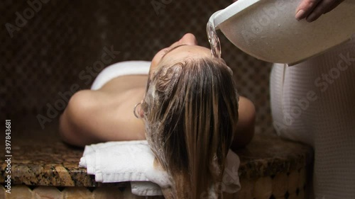 Woman masseur washes off the foam from the head of the blonde in a hammam. Foam in the Turkish bath. photo