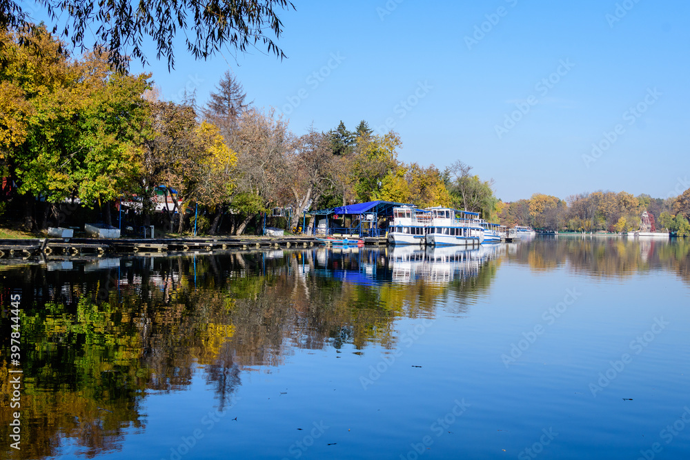 Landscape with white boats on Herastrau lake and large green trees in Herastrau Park in Bucharest, Romania,  in a sunny autumn day.