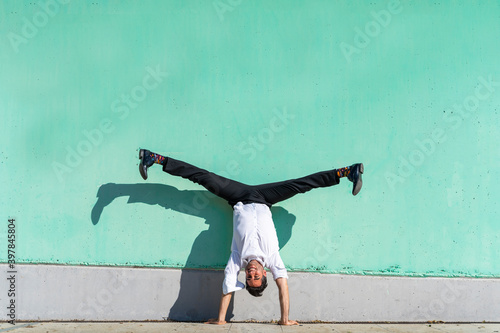 Businessman doing straddle handstand against green wall